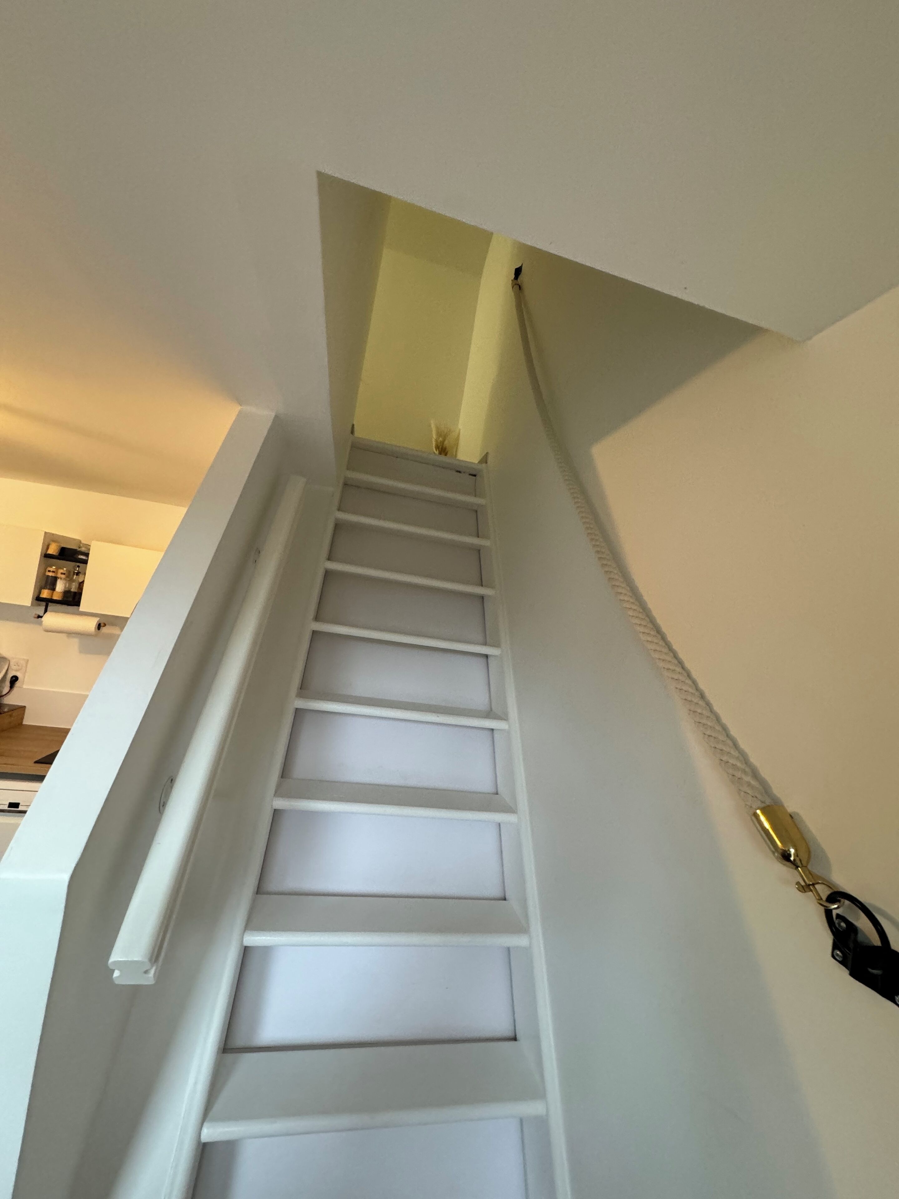 Un escalier avec des marches blanches et une rampe, menant à l’étage supérieur.