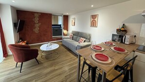 Una sala moderna con un sofá gris, un sillón rojo y una mesa de centro redonda. Se ha dispuesto una mesa de comedor con platos y vasos rojos.