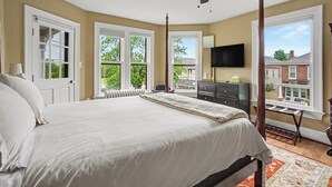 A bedroom with a large bed, a ceiling fan, a radiator, a TV, and a view of the outside. - Gettysburg Home sleeps 10 with parking and Game Room.  Just off the square. (Gettysburg)