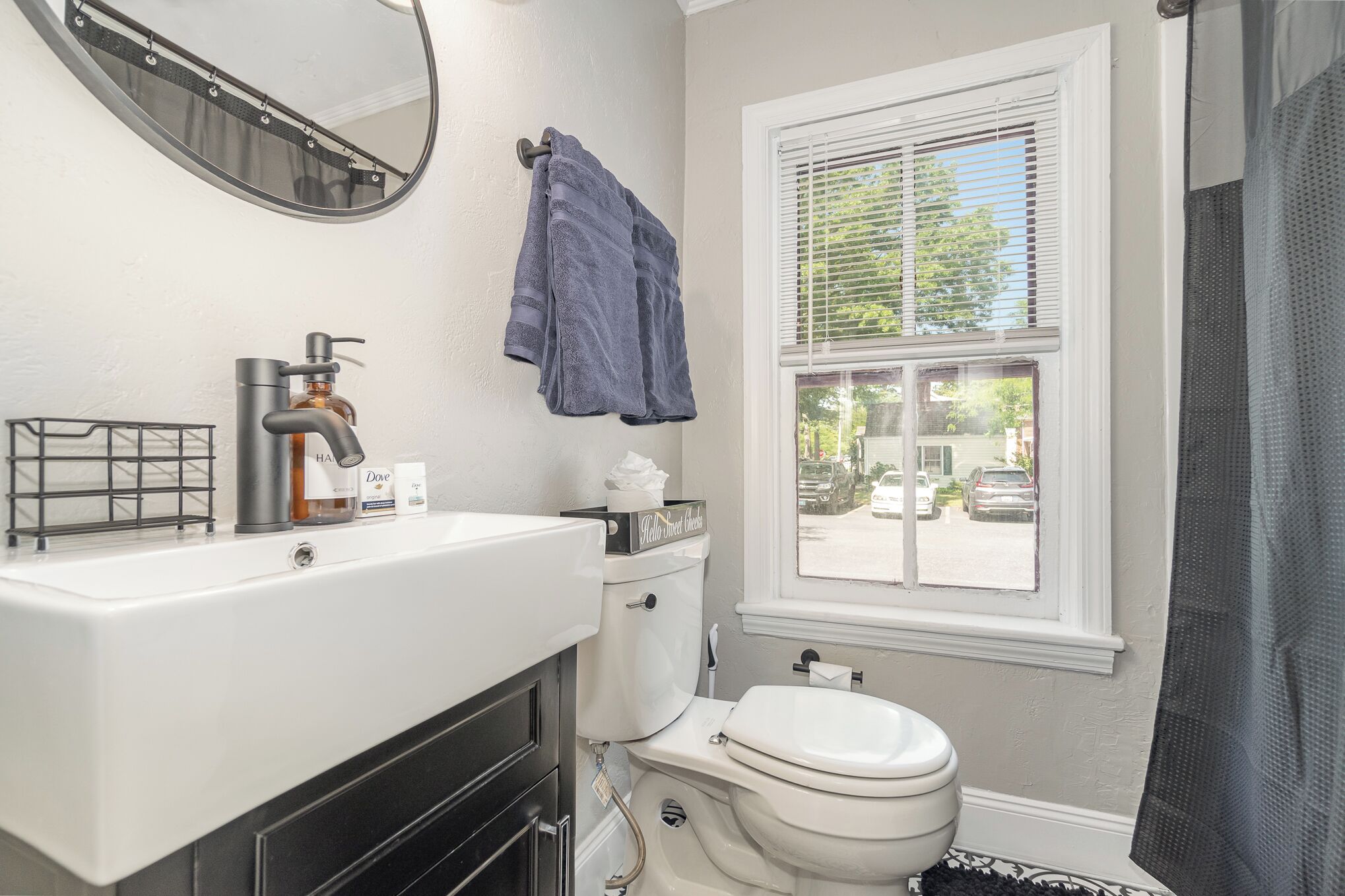A bathroom with a white sink, a toilet, a window with blinds, and a towel hanging on the wall.