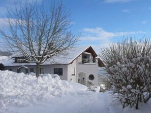 A two-story house with a balcony, surrounded by snow-covered ground and trees. - Holiday Apartment Resch (Perlesreut)