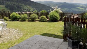 Een terras met een stenen vloer, een houten omheining en uitzicht op een bergachtig landschap.