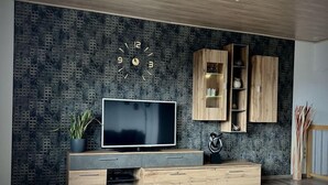Een moderne woonkamer met een grote flatscreen-tv, houten kasten en een wand met een honingraatmotief.