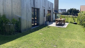 Ein modernes Gebäude mit Holzfassade, einem großen Fenster und einer Terrasse mit Tisch und Stühlen.