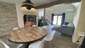Ein Essbereich mit einem runden Holztisch, weißen Stühlen und einer Blumenvase. Eine Backsteinwand und eine Treppe, die in einen anderen Raum führen.