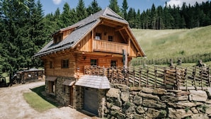 A wooden log cabin with a balcony, surrounded by a stone wall and a wooden fence.