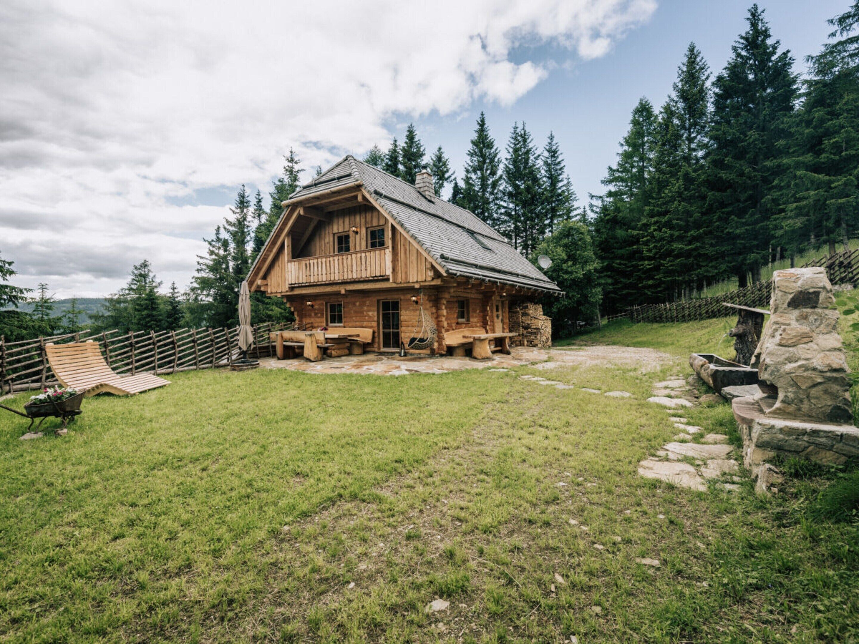 A wooden cabin with a balcony, surrounded by a stone wall and a wooden fence.