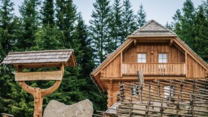 A wooden cabin with a balcony, surrounded by a wooden fence and a stone marker.