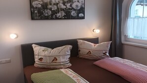 A bedroom with a bed, two pillows, a bedside table, a wall-mounted picture, and a window with curtains. - Apartment in Tyrol Near Ski Slopes (Fliess)