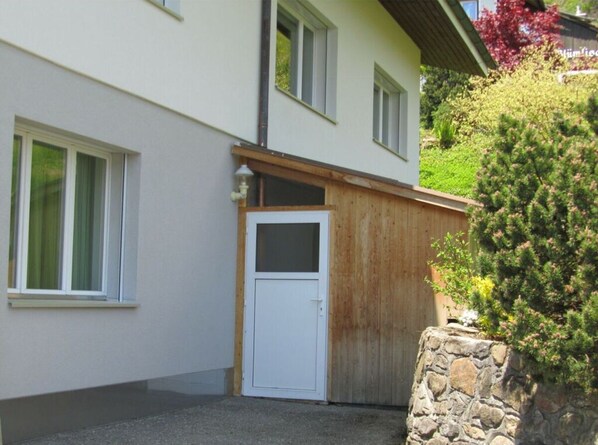 A building with a white exterior, a wooden door, and a stone wall. - Apartment Chalet Beatrice Share (Beatenberg)