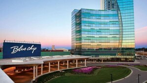 Un hôtel moderne doté d’une façade en verre incurvée, d’une enseigne « Blue Chip » bien visible et d’une cour aménagée.