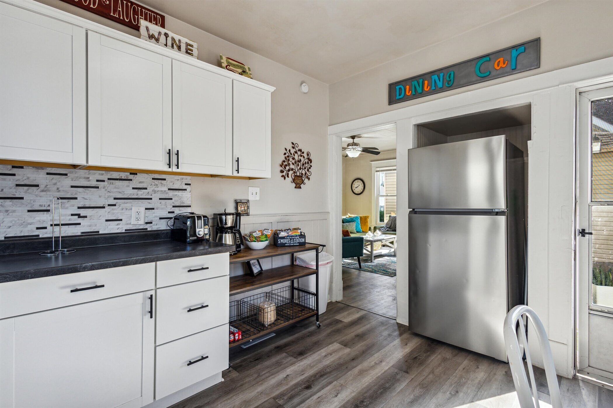 A kitchen with white cabinets, a marble backsplash, a stainless steel refrigerator, and a sign that reads "Dine Car".