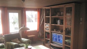 A living room with a sofa, a table with a plant, a television on a stand, and a wooden cabinet with shelves. - Holiday Home Monkfish House (Warin)