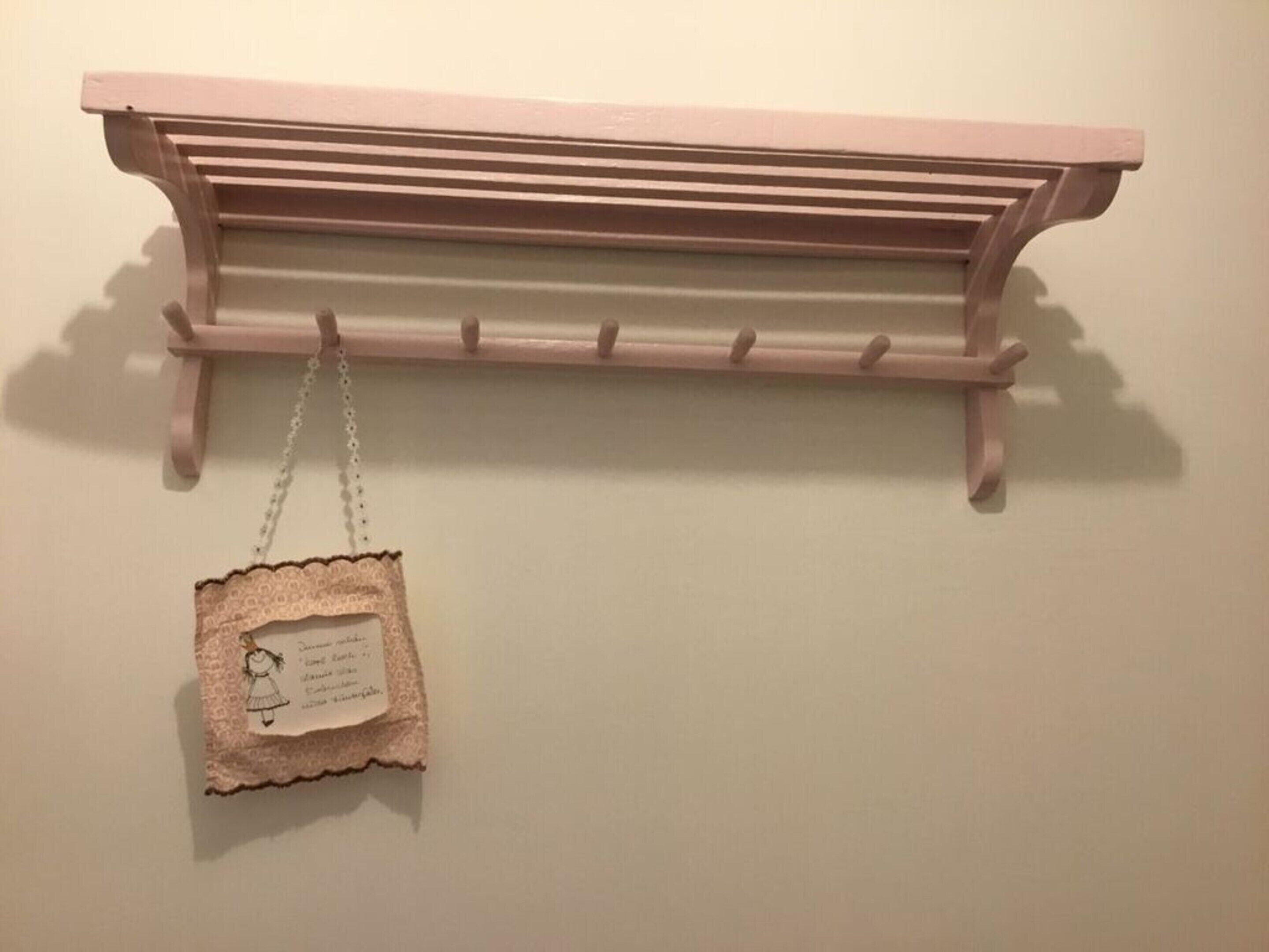 A pink wooden shelf with a lace tag hanging from it.