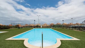 A rectangular swimming pool with a metal safety rail in the center, surrounded by well-maintained green grass. - Spacious Vacation Home in Corralejo (La Oliva)
