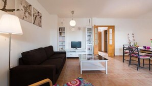 A modern living room with a sofa, coffee table, and TV. There is a dining area with chairs and a table. - Spacious Vacation Home in Corralejo (La Oliva)