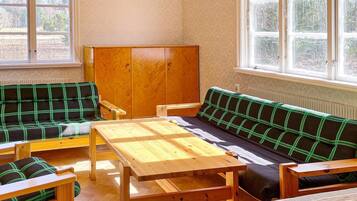 Una habitación con una mesa de madera, dos sofás verdes a cuadros y un armario de madera.