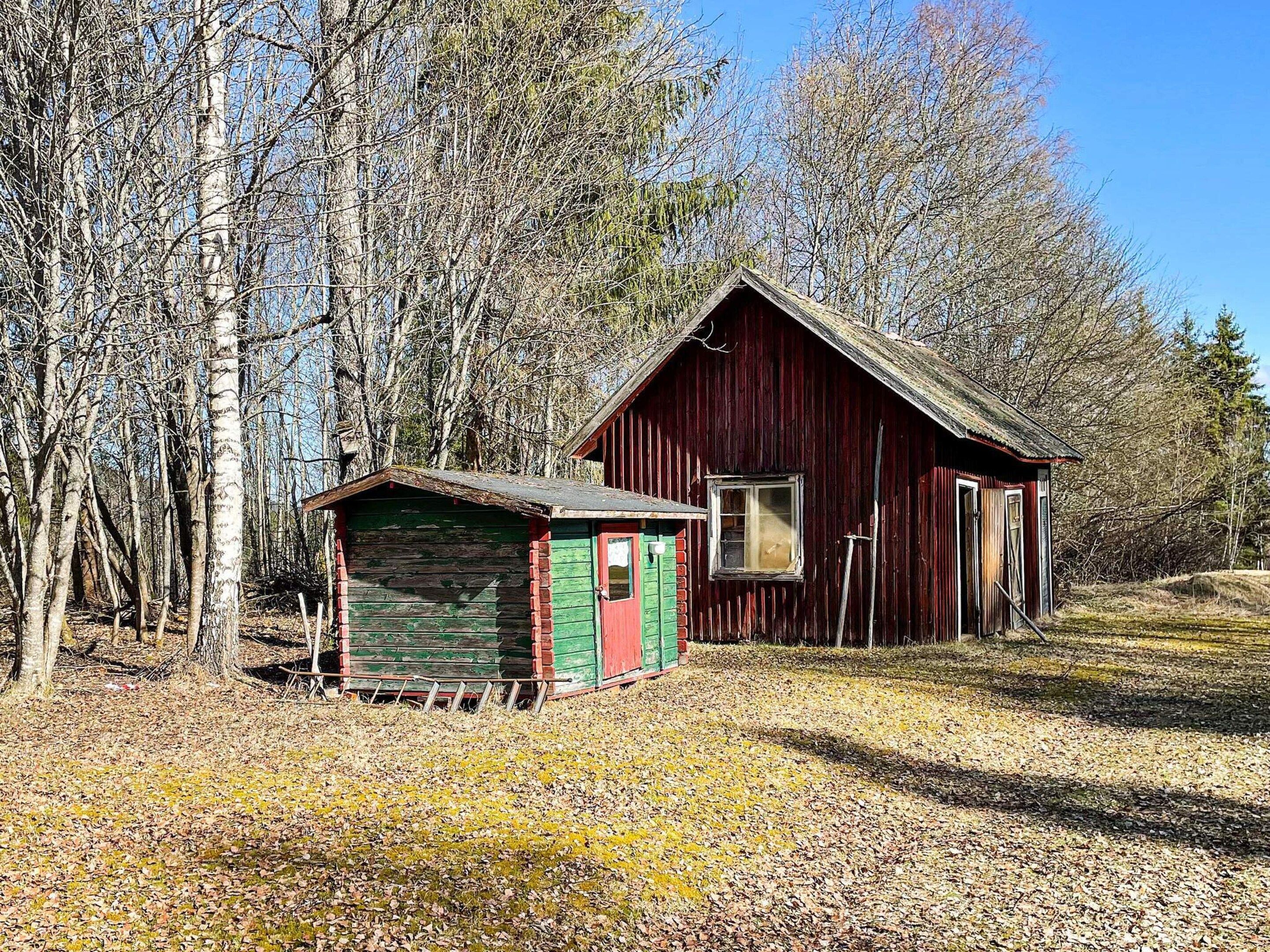 Une cabane en bois rustique, avec un abri de jardin vert, située dans une zone boisée.