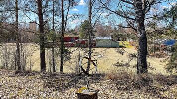 A forested area with a bicycle leaning against a tree, a fire truck in the background, and a building with a red roof.