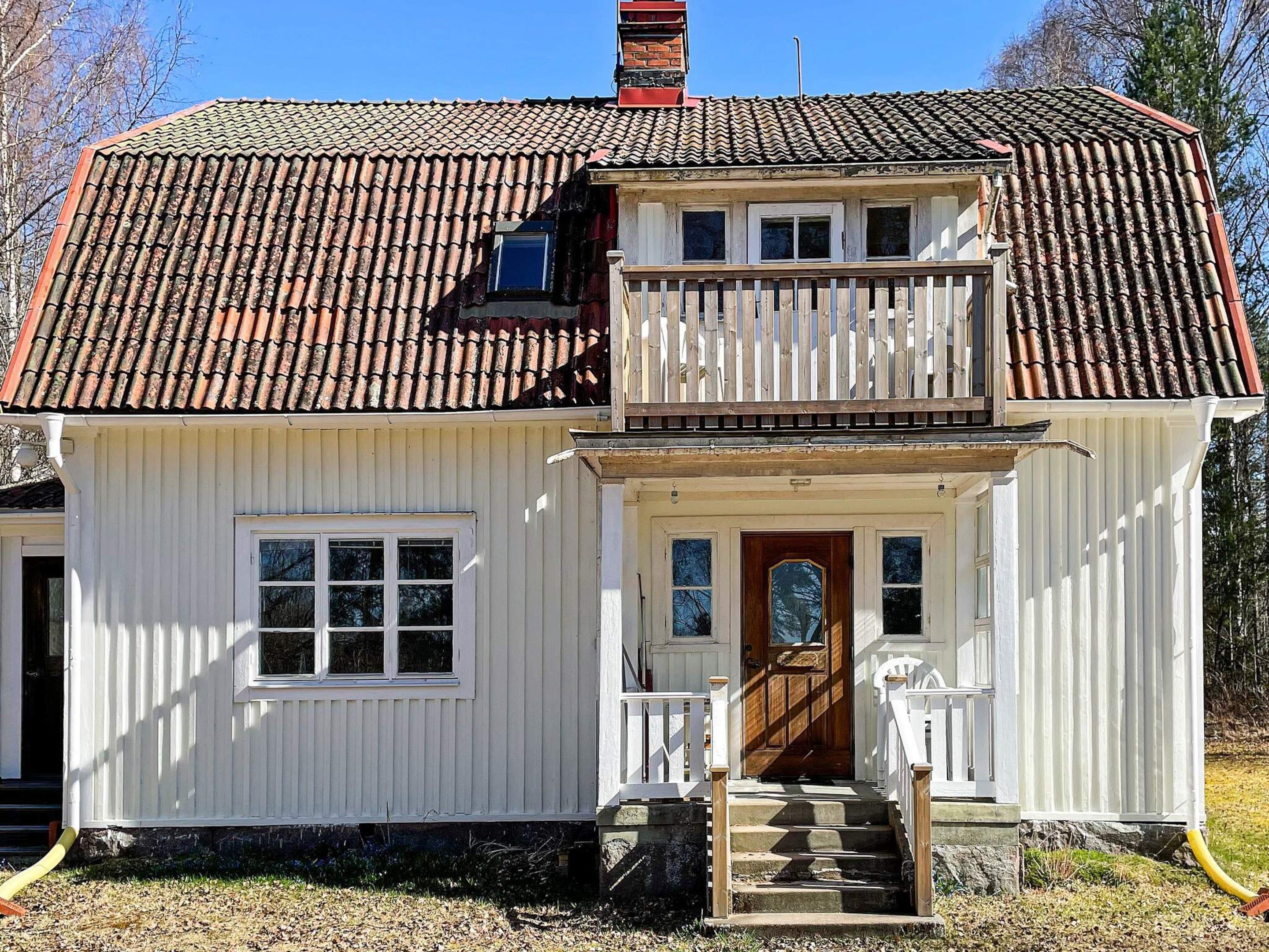 A two-story white house with a red-tiled roof, a wooden front porch, and a small balcony.