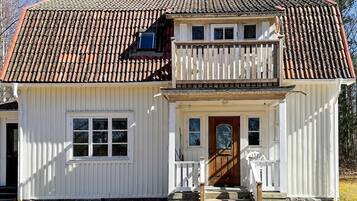 A two-story white house with a red-tiled roof, a wooden front porch, and a small balcony.