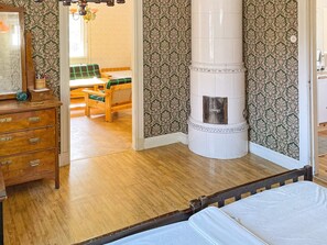 A bedroom with a wooden dresser, a bed, a white column, and a view into another room with a table and chairs.