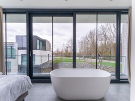 A modern bathroom with a freestanding bathtub, large sliding glass doors, and a view of a landscaped garden and neighboring buildings.