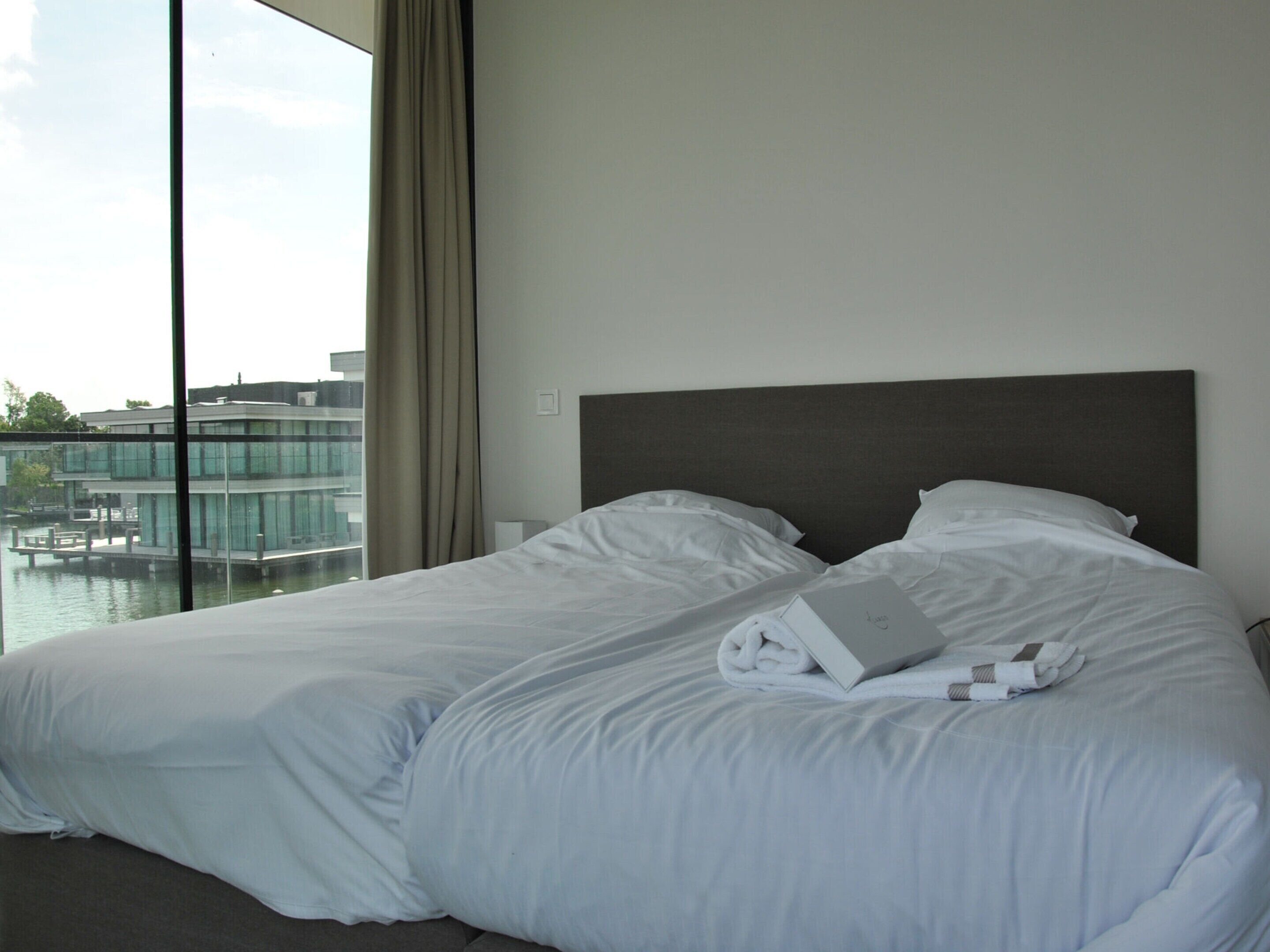 Habitación de hotel con una cama grande, vista a un edificio a través de un cuerpo de agua y una ventana con cortinas.