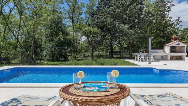 A poolside area with a wicker table, two glasses of water with lemon slices, and a magazine titled "ISTREN". - Large Holiday Home With Swimming Pool (Labin)