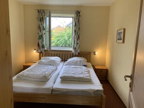 A small bedroom with two single beds, a window with curtains, bedside lamps, and a framed picture on the wall. - Holiday Home Beach and Nature (Gelting)