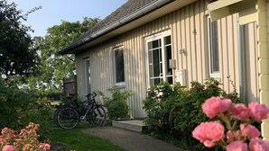 A house with a front porch, a bicycle parked outside, and a garden with pink flowers. - Holiday Home Beach and Nature (Gelting)
