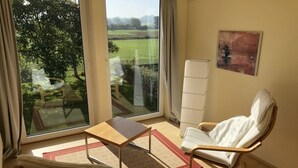 A room with a large window, a chair, a small table, and a floor lamp. - Holiday Home Beach and Nature (Gelting)