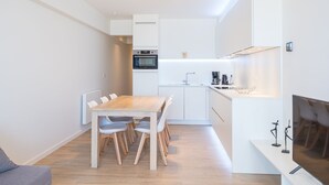 A modern kitchen with white cabinetry, a built-in oven, and a coffee maker. - Modern Apartment on the Seafront (Middelkerke)