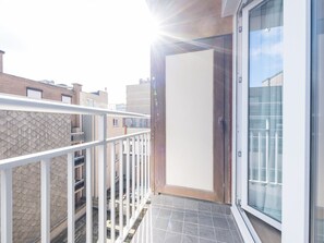 A balcony with a white railing, a sliding glass door, and a view of neighboring buildings. - Modern Apartment on the Seafront (Middelkerke)