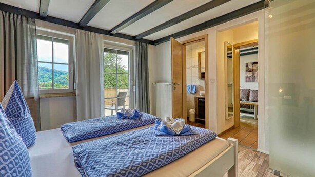 A bedroom with two beds, a window, and a bathroom visible through an open door. - Holiday Apartment Haus Leutner Bavarian Forest (Bodenmais)
