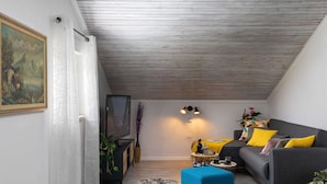 A modern living room with a grey sofa, a blue ottoman, and a TV on a wooden stand. - Apartment Tete Mare (Dubrovnik)