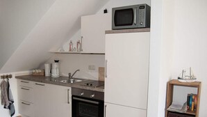 Une cuisine compacte équipée d’un four à micro-ondes, d’un four traditionnel, d’un évier et d’une petite étagère en bois où sont rangés des livres.