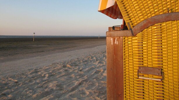 Une structure en bois située au bord de la plage, dotée d’un siège jaune tressé et d’une poignée en métal.