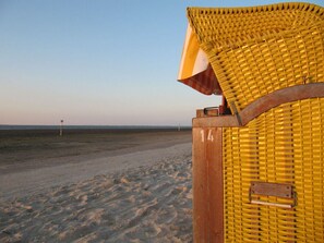 Une structure en bois située au bord de la plage, dotée d’un siège jaune tressé et d’une poignée en métal.