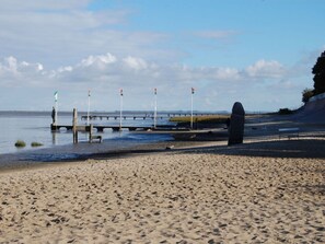 A sandy beach with a pier extending into the water, featuring several flags and a large stone structure. - Holiday Home Kleiner Friese Dangast (Varel)