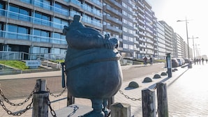A large bronze statue of a figure with a sack, located in front of a modern high-rise building with balconies and a sign reading "BRISBANE I". - Seaview Apartment, Middelkerke (Middelkerke)
