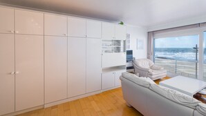 A modern living room with a large white sofa, a small white table, and a view of the ocean through large windows. - Seaview Apartment, Middelkerke (Middelkerke)