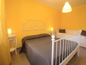 Ein Schlafzimmer mit einem Einzelbett, einem weißen Kopfende, einem Nachttisch mit Lampe und einem weißen Sofa.