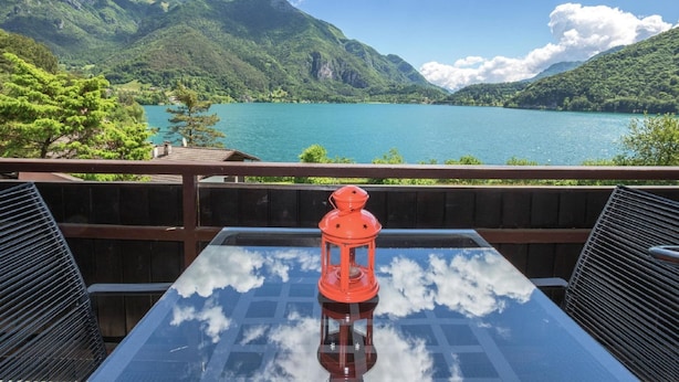 A table with a glass top and a red lantern, overlooking a lake with mountains in the background. - Belvilla by OYO Modern Holiday Home With Garden (Ledro)