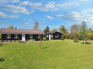 A two-story wooden house with a fenced yard, surrounded by trees and a clear sky. - 6 Person Holiday Home in Rodvig Stevns (Rodvig Stevns)