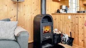 A cozy room with a wood-burning stove, a sofa, a lamp, and a kitchen area with shelves. - 6 Person Holiday Home in Rodvig Stevns (Rodvig Stevns)