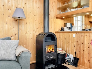 A cozy room with a wood-burning stove, a sofa, a lamp, and a kitchen area with shelves. - 6 Person Holiday Home in Rodvig Stevns (Rodvig Stevns)