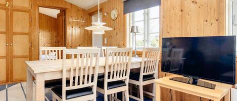 A wooden-paneled room with a dining table, chairs, a television, and a lamp.