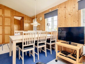 A wooden-paneled room with a dining table, chairs, a television, and a lamp.