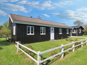 A black wooden building with a tiled roof, a white fence, and a grassy yard. - 6 Person Holiday Home in Rodvig Stevns (Rodvig Stevns)
